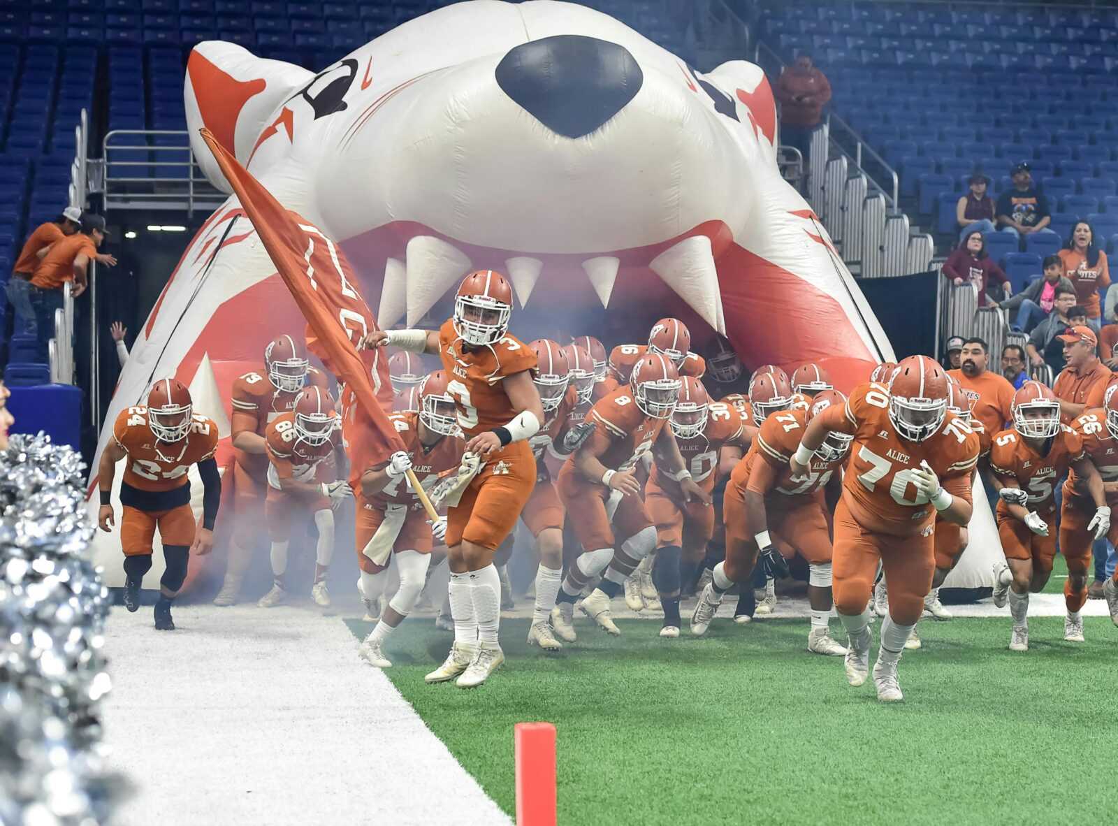 A dynamic scene of an American football team entering the stadium with enthusiasm, leading with a flag.